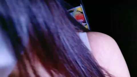 Media: A close-up video of a person with long, straight brown hair, showing a colorful sticker on the shoulder. The background is dark and out of focus, emphasizing the texture of the hair and the bright sticker.