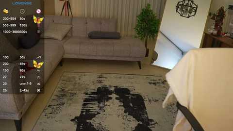 Media: Video of a modern living room with a beige sectional sofa, a large abstract painting on the floor, and a small potted plant in the corner.