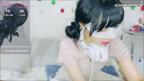 Media: Video of an Asian woman with black hair, wearing a white mask, playing a video game in a bright room.