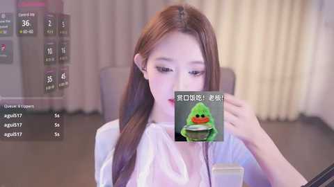 Media: A young Asian woman with long brown hair, fair skin, and subtle makeup, wears a white blouse. She holds a green emoji cup, set against a blurred indoor background.