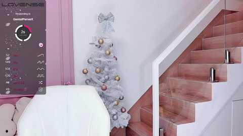 A video of a minimalist, pink-themed room with a white Christmas tree adorned with silver and gold baubles and a pink staircase.