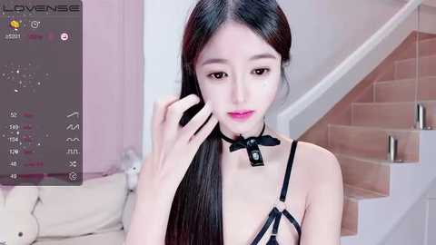 Media: Video of an East Asian woman with long black hair, fair skin, wearing black lingerie, standing in a modern, pink-toned living room with a beige couch.