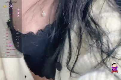 Media: A close-up video of a woman's hand holding a black lace bra, with long, dark hair cascading down her back. The background is blurred, showing a light-colored wall.