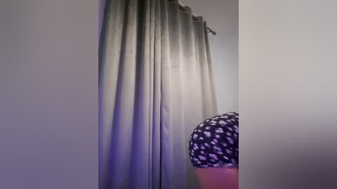 Media: Video of a person with a curvy, round buttocks clad in a black and white polka-dotted dress, standing in front of a light gray curtain in a dimly lit room.