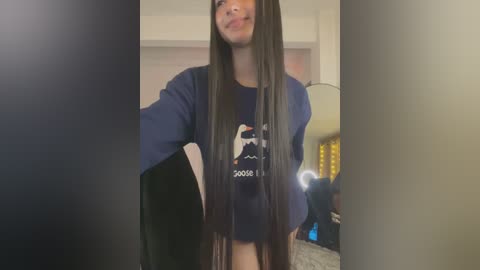 Media: Video of a young woman with long, straight black hair, wearing a navy blue hoodie with a Star Wars character logo, standing in a dimly lit room with a camera flash partially obstructing the image.