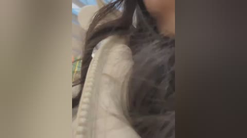 Media: A blurred video showing a person with long dark hair and a grey sleeve, holding a white, textured cushion. The background is out of focus, featuring a soft, muted color palette.