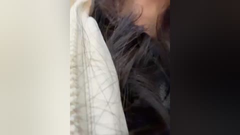 Media: Video of a person with dark hair, wearing a black shirt, lying on a white bedspread with a diamond pattern, blurred background.