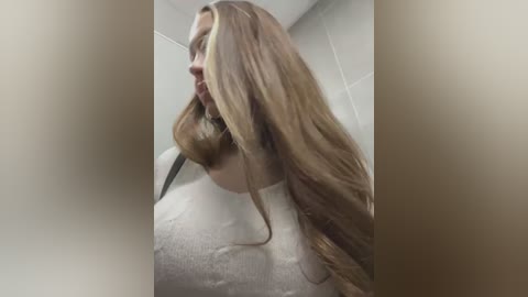 Media: Video of a woman with long, wet, blonde hair, wearing a white lace dress, in a bathroom with tiled walls.