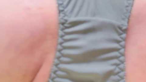 Media: Video of a woman's lower torso in a grey, ribbed, textured bodysuit. The skin tone is fair, and the fabric appears slightly wrinkled. The image focuses on the midsection, emphasizing the fabric texture and slight folds.