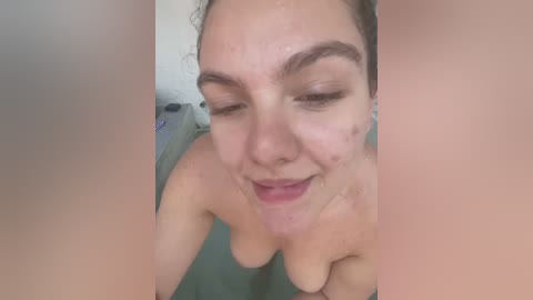 Media: Video of a young, light-skinned woman with wet hair, wearing makeup, smiling with closed eyes, and a slight blush on her cheeks, taken in a bathroom.