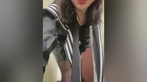 Media: Video of a person with medium skin tone, wearing a black and white striped jacket with a black tie, red lipstick, and shoulder-length dark hair.