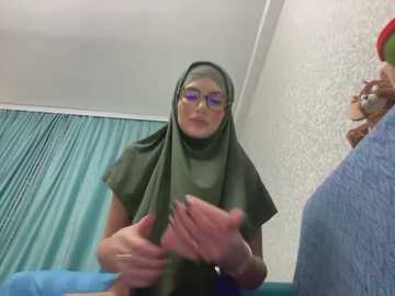 Media: A video shows a middle-aged woman in a green hijab and glasses, gesturing with her hands, standing in a hospital room with teal curtains and a textured wallpaper.