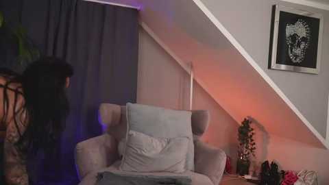 Media: Video of a modern living room with a dark gray armchair, a potted plant, and a framed art piece on a white wall, illuminated by ambient lighting.