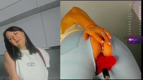 Media: Video of a woman with long black hair, wearing a white T-shirt, standing in a modern kitchen. She has a red dildo in her hand, pressing it against her blue jeans.