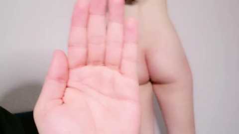 Media: A close-up video of a pale-skinned hand with fingers spread, raised, and slightly blurred against a plain white background. The hand is positioned centrally in the image, with a subtle shadow indicating a light source from the left.