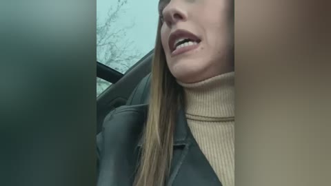 Media: A video of a close-up of a woman's face and upper body, wearing a black leather jacket and beige turtleneck, seen from a side angle through a car window, with blurred, leafless tree branches visible in the background.