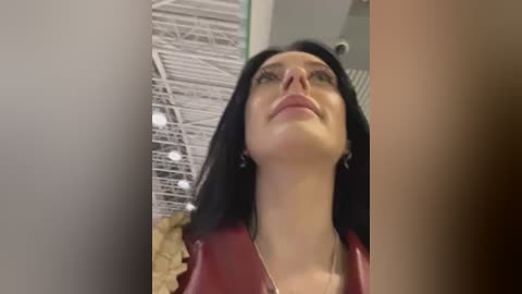 Media: A video of a woman with long black hair, fair skin, and a maroon leather jacket, standing in an industrial setting with a white ceiling and exposed beams.