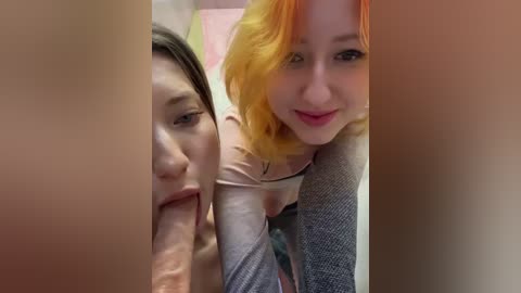 Media: Video of two women with pale skin and light makeup, one with shoulder-length blonde hair and the other with short dark hair, both performing oral sex on a large, erect penis.