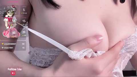 Media: A close-up video of a light-skinned woman with medium-sized breasts, wearing a white lace bra, being pulled down by a hand. The background includes a live-stream overlay with a virtual character, indicating an online livestream context.