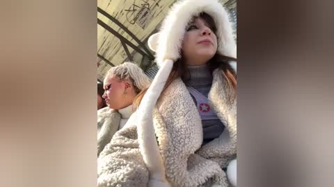 Media: Video of two women in winter clothing: one in a fluffy white coat, the other in a grey knit sweater. They are seated on a subway car with graffiti-covered walls.