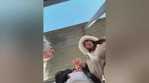 Media: Video of two young women with long hair, one in a white fur hat, the other in a white beanie, laughing and embracing in a sunlit room with a glass roof.