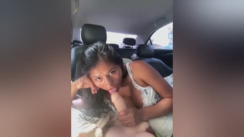 Media: A video shows a young woman with medium skin tone, dark hair, and a white lace top, performing oral sex on a man's erect penis in the backseat of a car.