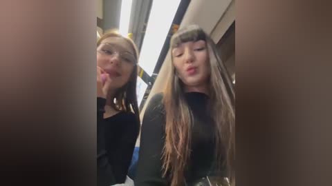 Media: A blurry video of two young women in a subway car, one licking her finger, the other making a kissing face. Both have long hair and wear dark clothes.