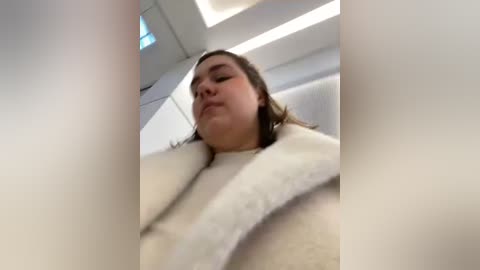 Media: A video of a woman in a white bathrobe, taken from a low angle, with a blurred background showing a modern, white room with a ceiling light.