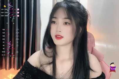 Media: Video of an Asian woman with long black hair, wearing a black off-shoulder dress, sitting against a blurred background. She has a pale complexion and red lipstick.