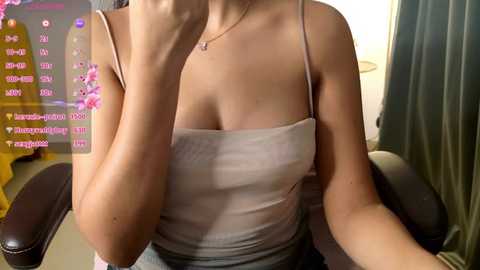 Media: Video of a light-skinned woman with medium-sized breasts wearing a tight, white tank top. She sits on a black leather chair, partially obscured by a pink overlay displaying social media metrics.