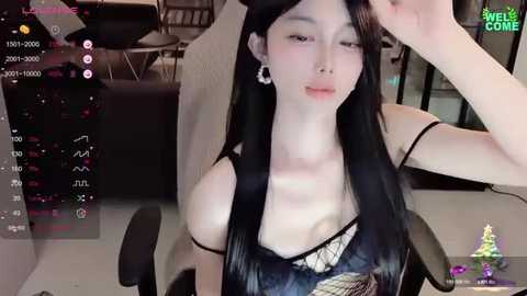 Media: A video of an East Asian woman with long black hair and pale skin, wearing a revealing black lace top, sitting in a modern chair. The background shows a dimly lit room with a computer screen displaying streaming software.