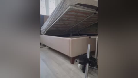 Media: Video of a partially constructed bed with a beige mattress and exposed wooden slats, situated in a room with light-colored wooden flooring and a partially visible window.