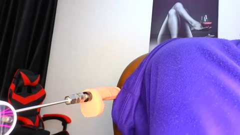 Media: Video of a person with a large, realistic sex doll strapped to their buttocks. The person is wearing a purple shirt and sitting on a black chair. A gaming chair with red accents is in the background.