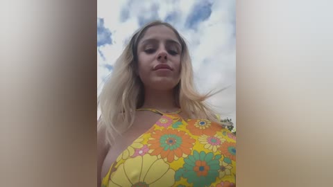 Media: Video of a blonde woman with a fair complexion, wearing a vibrant, floral-patterned yellow halter top, set against a cloudy sky background.