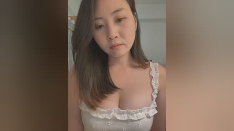 Media: Video of an Asian woman with straight, shoulder-length dark hair, wearing a white, ruffled, sleeveless dress, with a medium bust, in a neutral indoor setting.