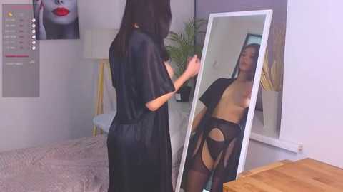 Media: Video of a woman in black lingerie, standing in front of a mirror in a bedroom, holding a phone.