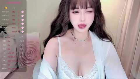 Media: A video of an East Asian woman with long, wavy black hair and fair skin, wearing a white lace bra and sheer robe, posing seductively in a bedroom with a floral wall decal and pink curtains.