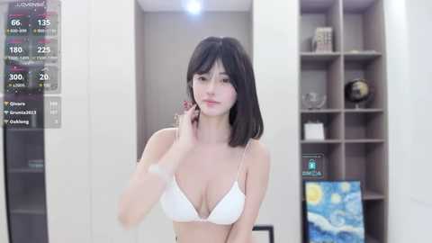 Media: A video of a fair-skinned woman with dark hair in a white bra, standing in a modern, minimalist room with a large digital screen displaying weather data.