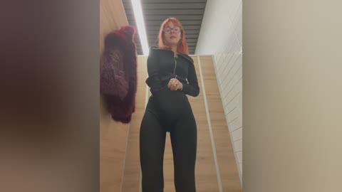 Media: Video of a red-haired woman in a black bodysuit, standing on a staircase with wooden walls, wearing glasses, holding a pink scarf.