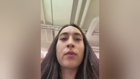 Media: Video of a young woman with long, straight black hair, fair skin, and full lips, captured in a close-up selfie from a slightly elevated angle. Background shows a white ceiling and bathroom fixtures.