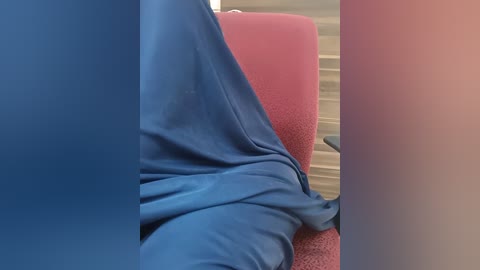 Media: Video of a person's upper torso, covered in blue and pink fabric, reclining on a red chair in a dimly lit room with white blinds.