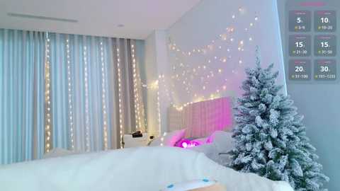 Video of a cozy, snow-themed bedroom with a white bed, light blue curtains, and a small snow-covered Christmas tree, adorned with fairy lights.