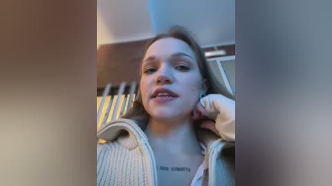 Media: Video of a young woman with light skin, light brown hair, and a tattoo reading \"Aim High\" on her chest, wearing a grey hoodie, leaning back in a chair, smiling.