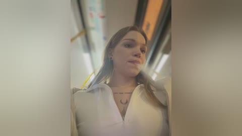 Media: Video of a young Caucasian woman with light brown hair, wearing a white blouse, inside a dimly lit subway car.