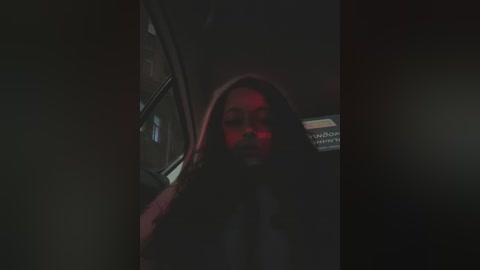 Media: A dimly-lit video shows a woman with long, dark hair and a red glow on her face, peering through a car window, hinting at an intimate or secretive moment.