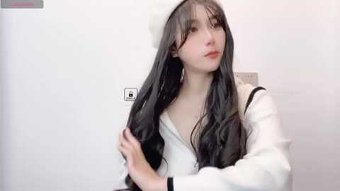 Media: A video of a young woman with long, straight black hair and pale skin, wearing a white beret and white sailor dress, adjusting her hair, against a plain white background.