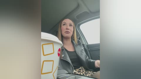 Media: A video of a blonde woman in a black leather jacket and leopard-print skirt, sitting in a car, holding a white cup with a red heart and yellow design.