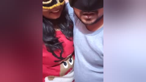 Media: Video of two people; woman with long black hair, wearing a red sweater with a reindeer design, black mask; man in light blue shirt, black mask, both smiling.