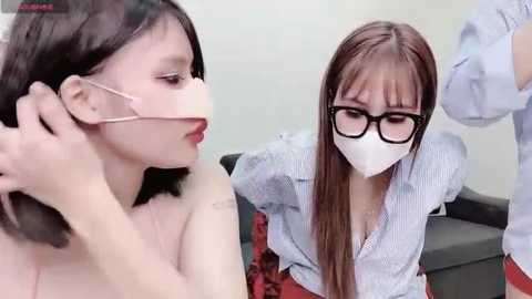 Media: Video of two Asian women with light skin, one adjusting a mask on the other's face, wearing glasses, seated in a clinical setting.