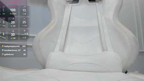 Media: Video of a white gaming chair with ergonomic design, adjustable armrests, and a sleek, minimalist aesthetic. In the background, a digital display shows gaming statistics.